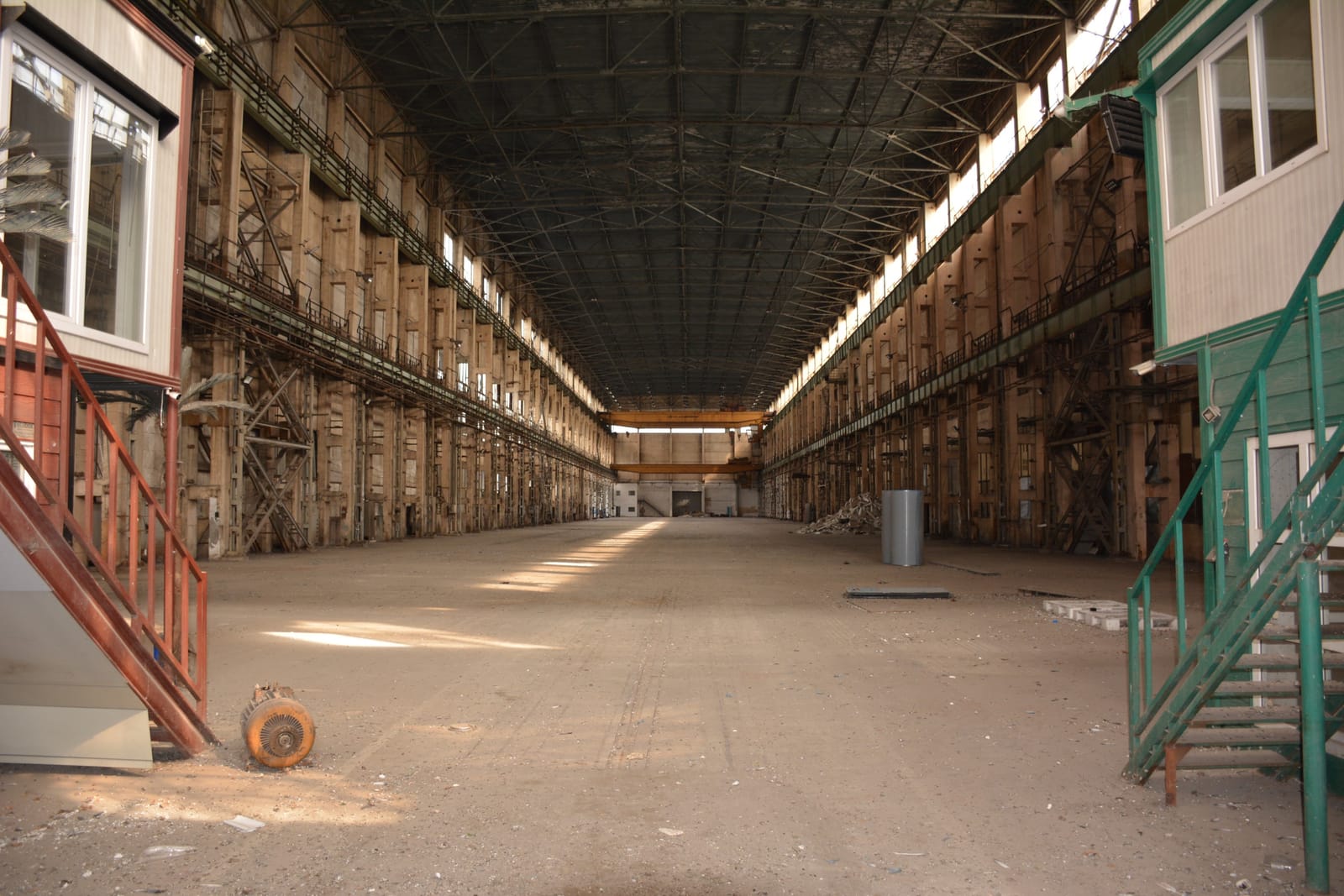 A vast industrial hangar with cathedral-like proportions. The space stretches endlessly, with tall concrete walls, rhythmic columns, and metal structures that create a sense of symmetry and infinity.